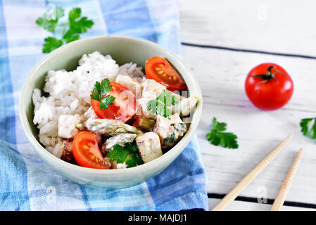 Delizioso piatto di tofu con il riso e i pomodori in una ciotola. Cibo Vegan con bacchette su un tavolo bianco. Stile di vita vegetariano. Foto Stock