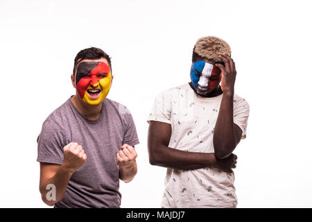 Felice tifoso di Germania celebrare la vittoria su sconvolto tifoso della Francia squadre nazionali con faccia dipinta isolato su bianco Foto Stock