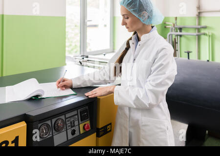 Donna ingegnere iscritto osservazioni sulle attrezzature e produzione Foto Stock