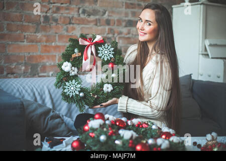 Giovane donna carina con Natale albero sempreverde Ghirlanda rosso con sfere di vetro, coni, nastro e Cannella a casa Foto Stock