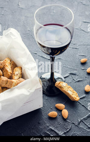 Italiani Tradizionali biscotti di mandorle cantuccini con un bicchiere di vino rosso su nero lo sfondo di pietra. Biscotti fatti in casa sul calcestruzzo scuro tavolo. Foto Stock