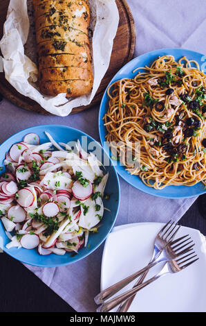 Cucina tradizionale italiana - Spaghetti alla puttanesca pasta con olive nere, tonno, acciughe, capperi, prezzemolo e insalata di verdure e cotto ciabatt Foto Stock