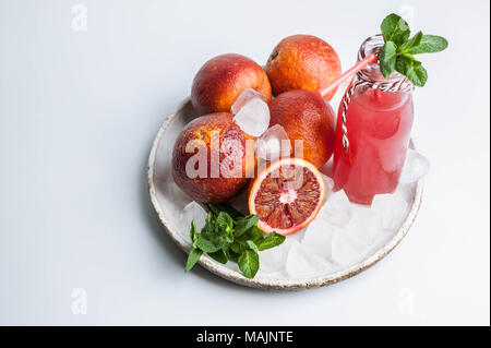 Arance sanguigne su una piastra e il succo in una bottiglia di vetro su uno sfondo bianco. Foto Stock