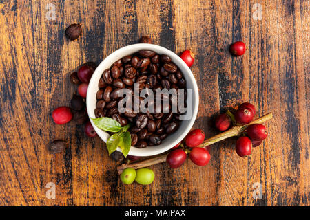 Caffè Fair trade background. Cofffea frutta, foglie, chicchi di caffè tostati dal di sopra su sfondo di legno. Foto Stock