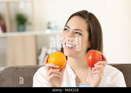 Donna felice chiedendo circa un apple e orange seduta su un divano nel salotto di casa Foto Stock