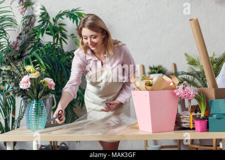 Immagine di un fioraio donna taglio di film al tavolo con fiori, carta Foto Stock