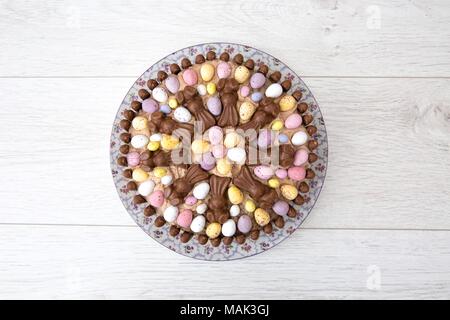 Guardando verso il basso a partire da sopra su una celebrazione di Pasqua torta decorata in mini uova di pasqua di cioccolato e caramelle su sfondo bianco Foto Stock