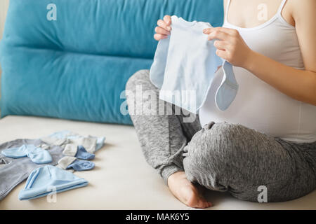 Primo piano della donna incinta la preparazione di vestiti del bambino. Donna incinta con abbigliamento per neonati. La gravidanza, persone, aspettativa del concetto di bambino Foto Stock