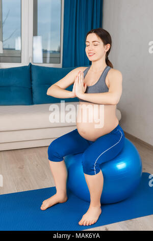 Felice donna incinta fare esercizio a casa. Donna incinta medita sul montare la sfera. Gravidanza gravidanza, yoga, uno stile di vita sano concetto Foto Stock