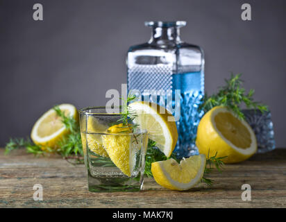 Con gin tonic e limone su un vecchio tavolo di legno . La bevanda alcolica con le fette di limone e il ramo di ginepro. Foto Stock