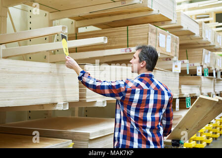 Uomo sceglie e acquista il legno compensato in un supermercato di costruzione Foto Stock