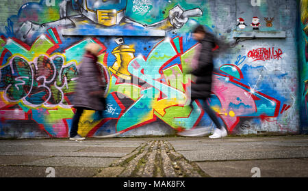 Persone sfocate oltrepassando un muro coperto di graffiti e arte di strada. Foto Stock