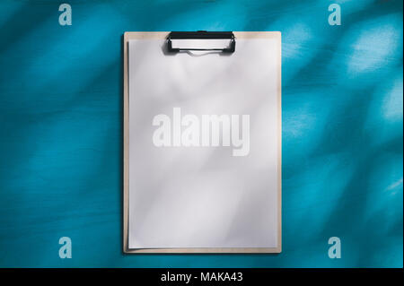 Dimensioni A4 negli appunti con il Libro bianco su blu tavolo in legno con illuminazione naturale effetto nella mattina tempo. sfondo con la zona vuota per il testo o messaggio. Foto Stock