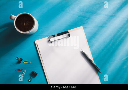 Dimensioni A4 negli appunti e una tazzina di caffè blu sulla tavola di legno con illuminazione naturale effetto nella mattina tempo. sfondo con la zona vuota per il testo o messaggio. Foto Stock