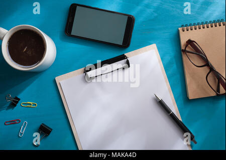 Dimensioni A4 appunti, smartphone piccolo taccuino, bicchieri e tazze di caffè blu sulla tavola di legno con illuminazione naturale effetto nella mattina tempo. background wit Foto Stock