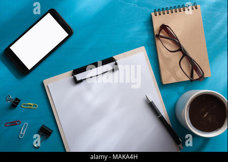 Dimensioni A4 appunti, smartphone piccolo taccuino, bicchieri e tazze di caffè blu sulla tavola di legno con illuminazione naturale effetto nella mattina tempo. background wit Foto Stock