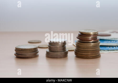 Tre pile di monete e fatture giacciono sul tavolo di legno. Foto Stock