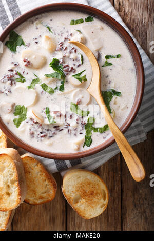 Zuppa cremosa di riso selvatico con funghi porcini close-up in una ciotola e toast sul tavolo. Verticale in alto vista da sopra Foto Stock