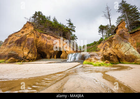 Abbraccio punto pieno a cascata da un inverno umido cade sulla roccia bassa e sulla spiaggia dove si svuota nel mare. Circondata su ciascun lato, da grandi s Foto Stock