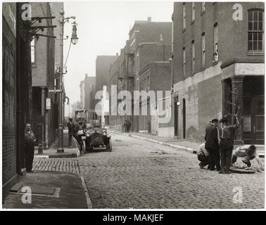 In orizzontale e di fotografia in bianco e nero che mostra un misterioso strada di ciottoli in corrispondenza di un angolo della seconda strada. Entrambi i lati della strada sono rivestiti con edifici in mattoni, variabile in altezza da due storie a quattro storie. Sul lato sinistro dell'immagine, un uomo è in piedi sull'angolo di strada sotto il cartello stradale per la seconda strada, mentre un altro uomo sorge accanto alla macchina parcheggiata sulla strada non identificato. Sul lato destro dell'immagine, un piccolo gruppo di uomini si sta abbassando una scaletta giù un tombino aperto. Nessun segni aziendali sono visibili, sebbene un segno per Stifel birra può essere visto al secondo angolo di strada. T Foto Stock