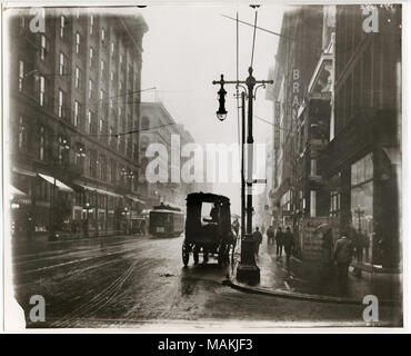 In orizzontale e di fotografia in bianco e nero che mostra Washington Avenue guardando ad est dalla settima strada in un giorno di pioggia. Molte aziende sono visibili lungo il lato sud di Washington, compreso il Barnum Hotel, un dentista office, Brandt, e un negozio di abbigliamento. Uno storefront offre un segno che pubblicizza, 'Baseball i punteggi per gli inning." Un carro chiuso è parcheggiato lungo il cordolo e un tram può essere visto in strada. Titolo: Washington Avenue guardando ad est dal 7 Street. . Tra il 1910 e il 1915. Holt, Charles Clemente, 1866-1925 Foto Stock