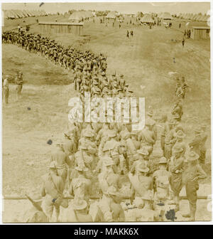 Verticale, seppia fotografia mostrante un folto gruppo di soldati in uniforme marciando in righe di quattro o cinque attraverso un campo verso una zona dove i filari di forma conica tende sono impostati. Altri uomini in uniforme sono in piedi fuori ai lati della marching soldati, osservando i loro progressi. Titolo: soldati che marciano in righe verso un campo di forma conica tende mentre altri guardano. . Tra circa 1914 e circa 1918. Michel, Carl Foto Stock