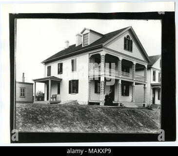 In orizzontale e di fotografia in bianco e nero di una a tre piani dipinto di bianco residenza in mattoni con finestre dormer e a due piani con portico frontale con il lavoro di reticolo. Ante Telaio ciascuna finestra sul primo, secondo e terzo livello. Ingresso laterale con una panca è visibile sotto un portico sul lato destro del residence. Due donne sono seduti e in piedi vicino al portico anteriore. Titolo: Webster, Dr. Asbel W. Residence. Michigan e Kraus angolo nordest. . Circa 1850. Swekosky, William G., 1895-1964 Foto Stock