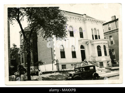 In orizzontale e di fotografia in bianco e nero di una di tre piani in pietra e mattoni con residenti cornicione e conci il rivestimento delle facciate laterali dell'edificio. Una finestra di baia con il cornicione è visibile sul lato destro della residenza accanto alla porta anteriore che è presente al di sotto modillions e una sporgenza. Il lato sinistro del residence dispone anche di una colonna di finestre a baia. Un uomo si siede sui gradini di fronte e tre donne sono visti nell'angolo inferiore sinistro della fotografia. Titolo: Wegler, Charles Residence. 1834 Kennett Place. . Tra circa 1878 e circa 1890. Swekosky, William G., 1895-1964 Foto Stock