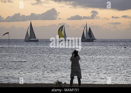 Honolulu, Hawaii, Stati Uniti d'America. 15 Dic, 2017. Una donna prende una foto delle barche a vela off Kaimana Beach, Honolulu, Hawaii. La spiaggia è noto anche come Sans Souci Beach ed è popolare tra la gente del posto e turisti. Credito: Bayne Stanley/ZUMA filo/Alamy Live News Foto Stock