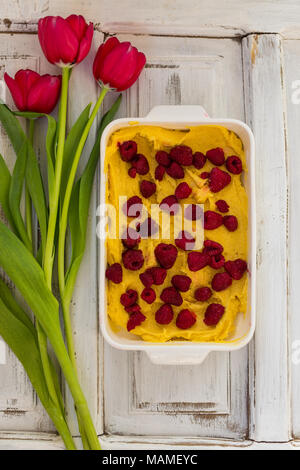 Vista superiore colpo di materie la torta di fragole in bianco forma di cottura con tulipani rossi dal suo lato in bianco da tavolo rustico Foto Stock