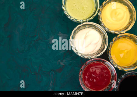 Set di diverse salse. Salse ketchup, senape, maionese, wasabi, salsa di soia in piccoli recipienti su sfondo verde Foto Stock