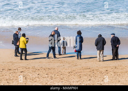 I turisti e visitatori di godersi il sole primaverile in piedi sul litorale a Fistral Beach in Newquay Cornwall. Foto Stock