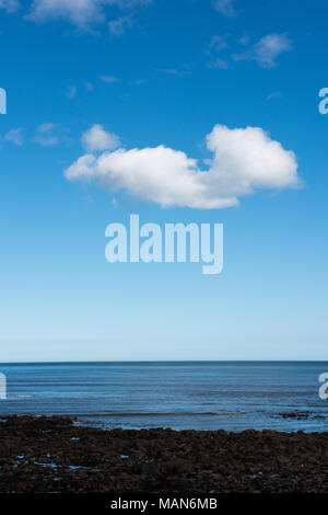 Costa rocciosa con bassa marea sotto un cielo blu brillante con nuvole sparse sulla costa del Regno Unito, rivelando pozze di marea e texture costiere Foto Stock