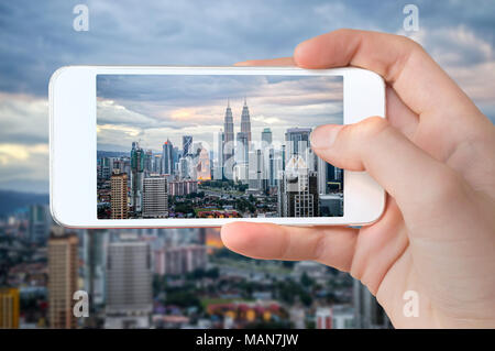 Primo piano di una mano con lo smartphone di scattare una foto dello skyline di Kuala Lumpur, Malesia Foto Stock