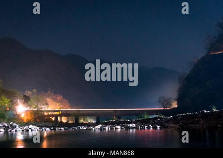 Night Shot del paesaggio con ponte su un fiume ancora e le montagne in distanza e riflessi nell'acqua. Girato a Haridwar rishikesh india. perfetto come un viaggio turistico shot Foto Stock