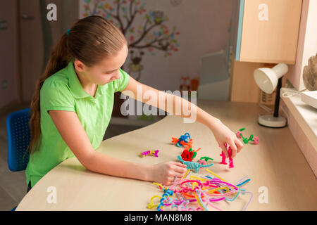 Carino bambina creazione di giocattoli con bastoncini di ciniglia al tavolo. La creatività e il concetto di fatti a mano. Foto Stock