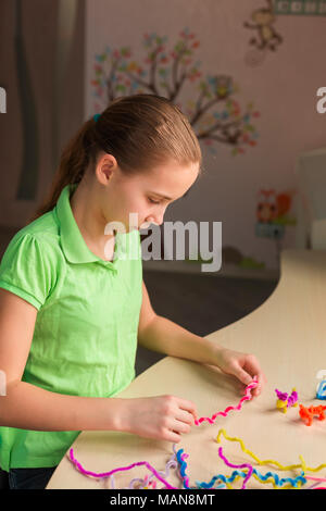 Carino bambina creazione di giocattoli con bastoncini di ciniglia al tavolo. La creatività e il concetto di fatti a mano. Foto Stock