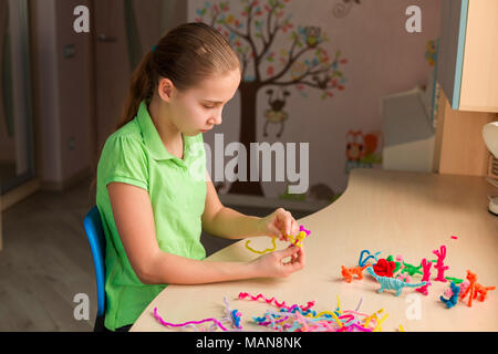 Carino bambina creazione di giocattoli con bastoncini di ciniglia al tavolo. La creatività e il concetto di fatti a mano. Foto Stock