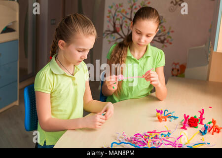 Carino bambine creazione di giocattoli con bastoncini di ciniglia al tavolo. La creatività e il concetto di fatti a mano. Foto Stock