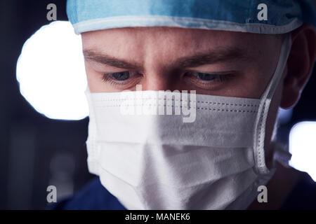 Maschio lavoratore del settore sanitario in scrubs, colpo alla testa, guardando verso il basso Foto Stock