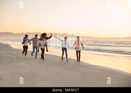 Gruppo di amici divertendosi in esecuzione lungo la spiaggia invernale insieme Foto Stock