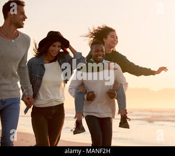 Gruppo di amici divertendosi in esecuzione lungo la spiaggia invernale insieme Foto Stock