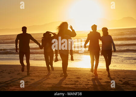 Silhouette di amici divertendosi in esecuzione lungo la Spiaggia Invernale Foto Stock