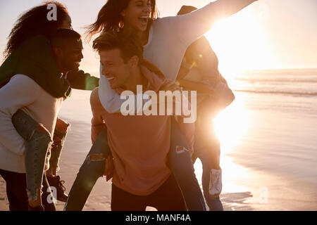 Gruppo di amici avente Piggyback gara sulla Spiaggia Invernale insieme Foto Stock