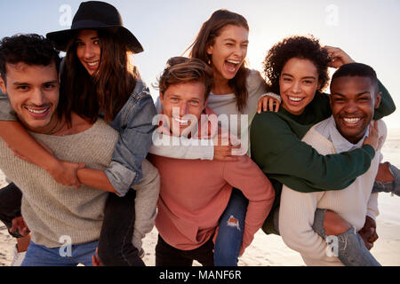 Ritratto di amici avente Piggyback gara sulla Spiaggia Invernale Foto Stock