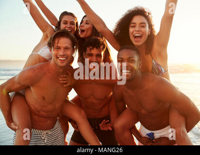 Gruppo di amici in vacanza avente Piggyback gara sulla spiaggia Foto Stock