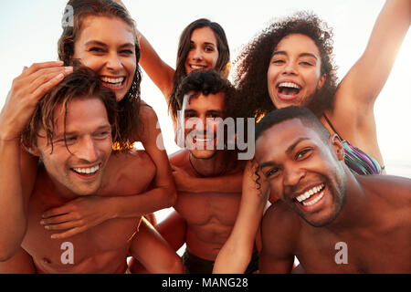 Gruppo di amici in vacanza avente Piggyback gara sulla spiaggia Foto Stock