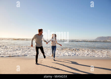 Giovane avendo divertimento lungo la spiaggia invernale insieme Foto Stock