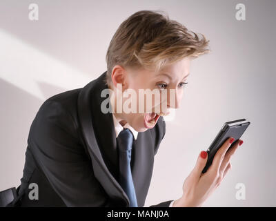 Infastiditi business donna in costume nero urlando in rabbia in smart phone. Foto Stock