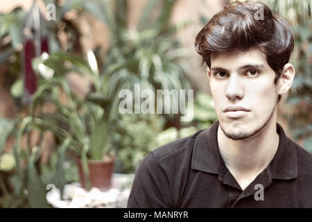 Ritratto di un giovane uomo che guarda la fotocamera, di pensare e di grave, all'esterno. Foto Stock